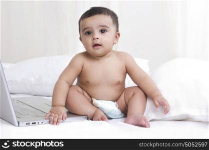 Baby sitting on bed with laptop