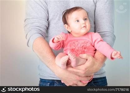 Baby sitting on fathers hands. Baby is wearing pink body suit and looking at right side