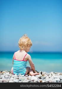 Baby sitting on sea shore. Rear view