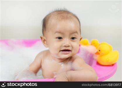 baby taking a bath in bathtub and playing with foam bubbles at home
