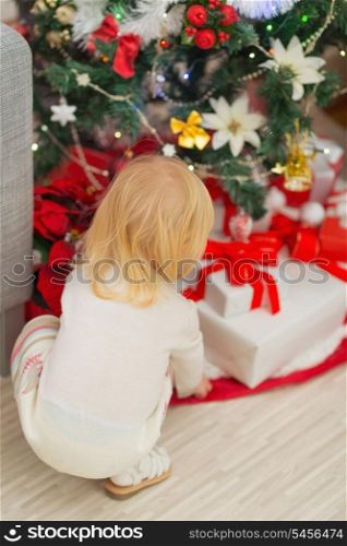 Baby taking Christmas present from under Christmas tree. Rear view