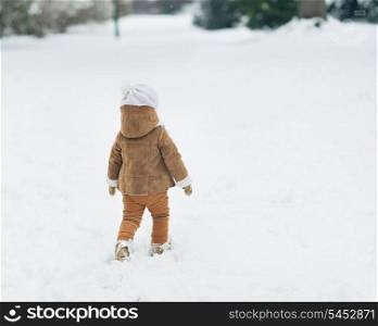 Baby walking in winter park . rear view