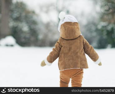 Baby walking in winter park . rear view