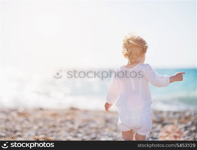 Baby walking on beach. Rear view