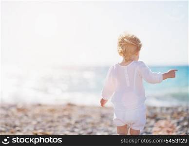 Baby walking on beach. Rear view