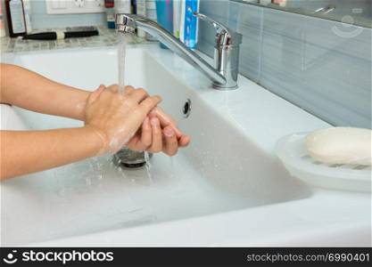 Baby washes soap from hands in washbasin