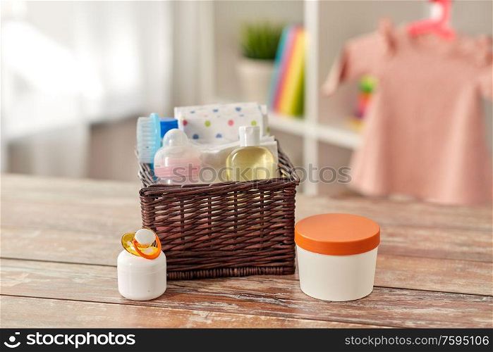 babyhood and care products concept - baby things in wicker basket on wooden table at home. baby things in basket on wooden table at home