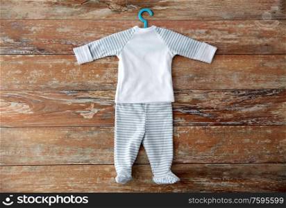 babyhood and clothing concept - baby clothes set of shirt and romper with hanger on wooden table. baby clothes set with hanger on wooden table