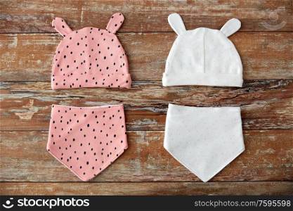 babyhood and clothing concept - baby hats with ears and bibs on wooden table. baby hats with ears and bibs on wooden table