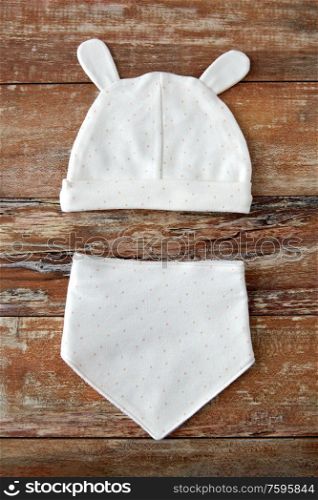 babyhood and clothing concept - white baby hat with ears and bib on wooden table. baby hat with ears and bib on wooden table