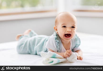 babyhood and people concept - crying little baby girl lying on white blanket. crying baby girl lying on white blanket