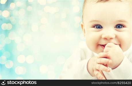 babyhood, childhood and people concept - happy baby face over blue holidays lights background