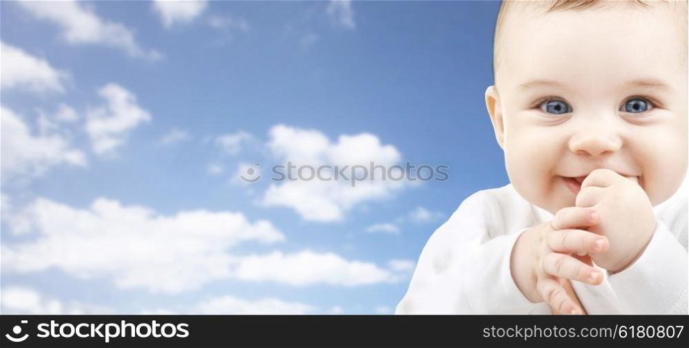 babyhood, childhood and people concept - happy baby face over blue sky background