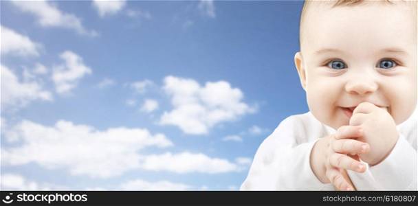 babyhood, childhood and people concept - happy baby face over blue sky background