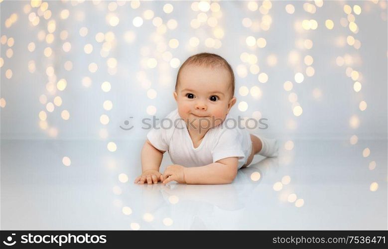 babyhood, childhood and people concept - sweet little baby lying on floor over festive lights background. sweet little baby lying on floor over lights