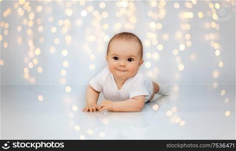 babyhood, childhood and people concept - sweet little baby lying on floor over festive lights background. sweet little baby lying on floor over lights
