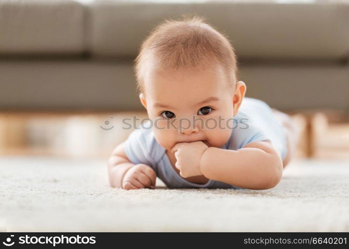 babyhood, childhood and teething concept - sweet little asian baby boy lying on floor at home. sweet little asian baby boy lying on floor at home