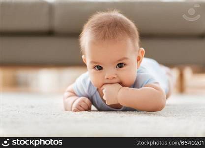 babyhood, childhood and teething concept - sweet little asian baby boy lying on floor at home. sweet little asian baby boy lying on floor at home