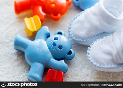 babyhood, childhood, toys, clothing and object concept - close up of baby rattle and bootees for newborn boy on towel