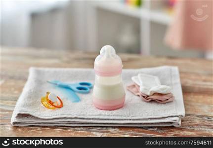 babyhood concept - bottle with baby milk formula and things on wooden table at home. bottle with baby milk formula and things on table