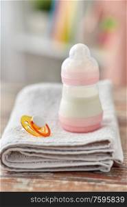 babyhood concept - bottle with baby milk formula, soother and bath towel on wooden table at home. bottle with baby milk formula, soother and towel