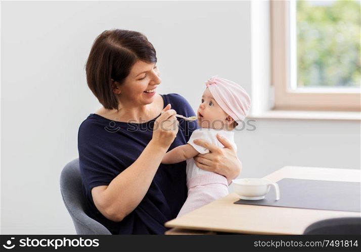 babyhood, motherhood and food concept - happy middle-aged mother spoon feeding baby daughter with puree at home. middle-aged mother feeding baby daughter at home