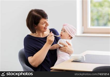 babyhood, motherhood and food concept - happy middle-aged mother spoon feeding baby daughter with puree at home. middle-aged mother feeding baby daughter at home