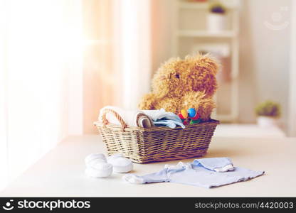 babyhood, motherhood, clothing and object concept - close up of baby clothes and toys for newborn boy in basket at home