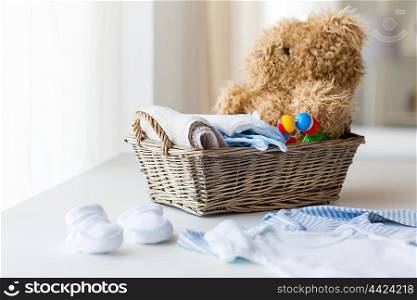 babyhood, motherhood, clothing and object concept - close up of baby clothes and toys for newborn boy in basket at home