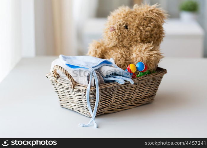 babyhood, motherhood, clothing and object concept - close up of baby clothes and toys for newborn boy in basket at home