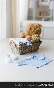 babyhood, motherhood, clothing and object concept - close up of baby clothes and toys for newborn boy in basket at home