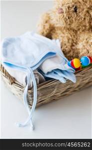 babyhood, motherhood, clothing and object concept - close up of baby clothes and toys for newborn boy in basket
