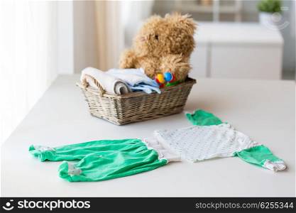 babyhood, motherhood, clothing and object concept - close up of baby clothes set and toys for newborn in basket at home