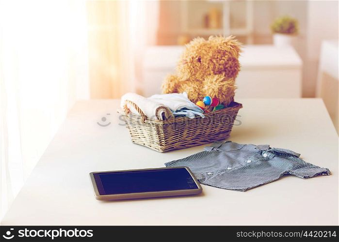 babyhood, motherhood, clothing, technology and object concept - close up of baby clothes and toys for newborn boy in basket with tablet pc computer at home