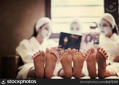 bachelorette party in spa, girls with face mask reading magazine, pedicure concept, foots with seperator in focus. bachelorette party in spa, girls with face mask reading magazine