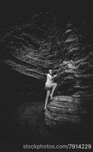 Back and white shot of beautiful woman climbing up the cliff on sea shore