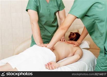 Back massage of woman in four hands by two massage therapists in massage salon.. Back massage of woman.