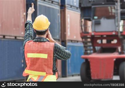 Back of caucasian Foreman or Engineer wearing safety helmet and control for loading containers while talking on walkie talkie. Engineering and Shipping Concept.