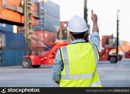Back of foreman or cargo container worker show thumbs up to other co-worker who control crane truck in workplace area. Logistic and shipyard transportation for delivery system concept.