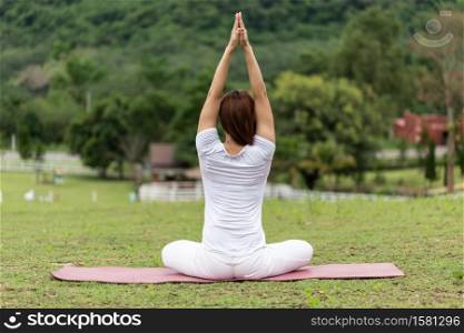 Back of view Asian woman sitting on yoga mat practice lotus pose with yoga meditation relax and refresh health on green grass feeling happiness and comfortable in garden,Healthcare concept