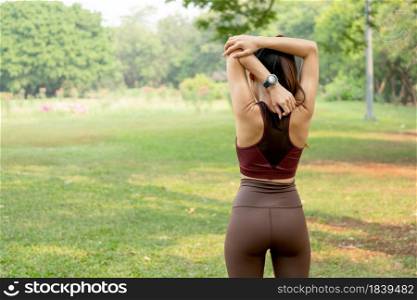 Back of woman do arm stretching and look to green field or tree after exercise in park or garden with daylight.