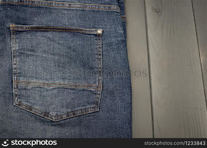 Back pocket of a washed blue denim trousers with gold stitching on gray wooden background