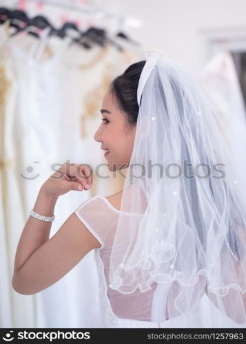 Back shot of asian bride checking her dress in dressing room.