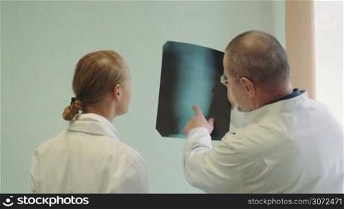 Back shot of man and woman doctors examining, discussing and comparing two knee x-rays images