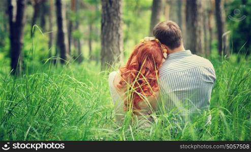 Back side of a peaceful couple sitting on a grass in the forest, enjoying beauty of nature, love and togetherness concept
