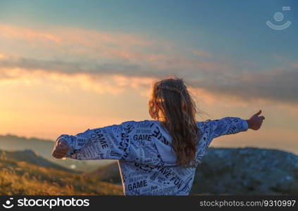 Back side of a teen girl having fun in the mountains. Happy child with raised up hands enjoying mild sunset light. Active kids. Healthy life.. Cheerful teen girl in the mountains