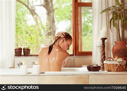 Back side of a woman in the bathtub washes her hair, dayspa in luxury spa hotel, hygiene and pleasure concept
