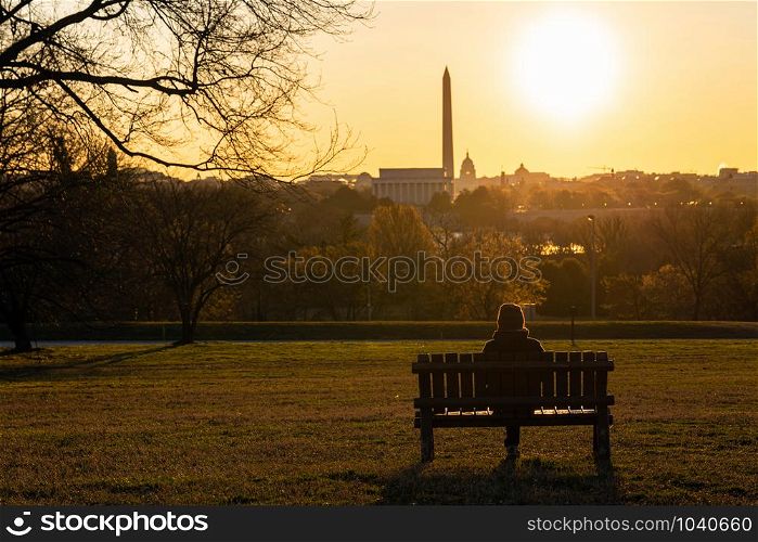 Back side of asian woman sitting alone over the Washington DC Landmark which can see United states Capitol, washington monument and lincoln memorial at the sunrise time, history and culture concept