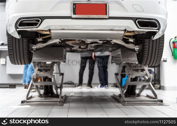 Back side of Car lifted in automobile service and Asian mechanic Checking and torch tire in maintainance service center which is a part of showroom, technician or professional work for customer concept