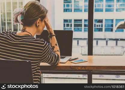 Back side of Depressed Hipster young Woman freelancer thinking about her job in serious action which have technology Laptop in the Loft cafe workplace. Creative Startup and entrepreneur business concept